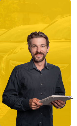 Ein Mann mit braunen Haaren und Bart, der ein dunkles Button-up-Hemd trägt, lächelt und hält ein Tablet in der Hand. Der Hintergrund ist gelb und zeigt schwache Bilder von Autos.