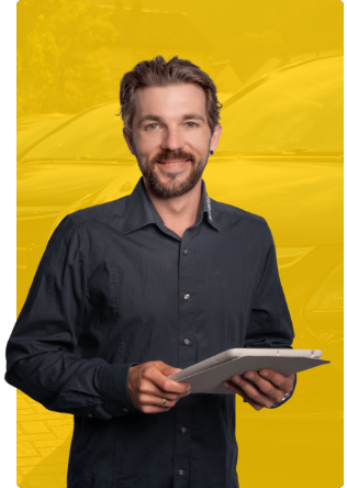 Ein Mann mit kurzen braunen Haaren und Bart, der ein dunkles Button-up-Hemd trägt, lächelt, während er ein Tablet vor einem hellgelben Hintergrund hält.